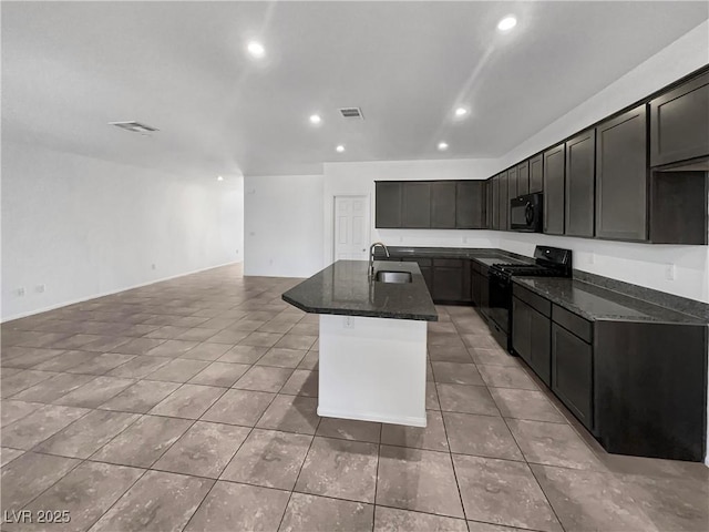 kitchen with a center island with sink, dark stone counters, recessed lighting, a sink, and black appliances