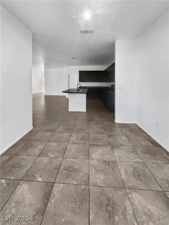 interior space featuring tile patterned floors, visible vents, a kitchen island with sink, dark countertops, and open floor plan