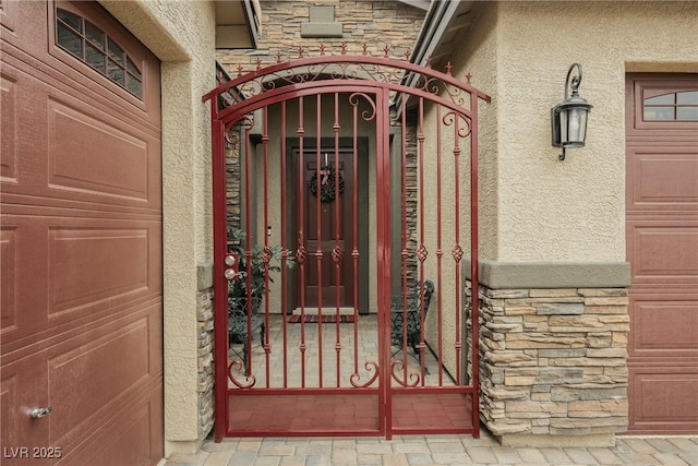 doorway to property with a garage, a gate, stone siding, and stucco siding