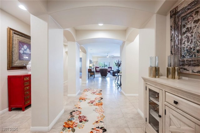 corridor featuring arched walkways, light tile patterned floors, and baseboards