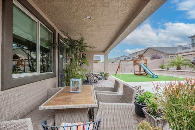 view of patio with a playground, outdoor dining area, and fence