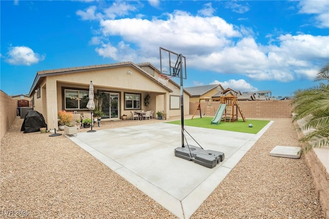 rear view of house with stucco siding, a playground, a fenced backyard, and a patio area