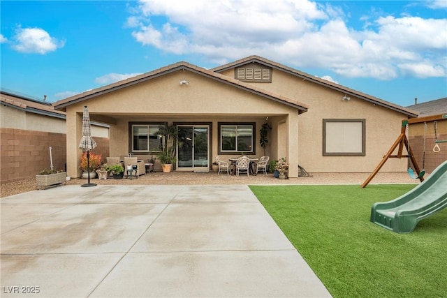 rear view of property featuring a patio area, stucco siding, a playground, and fence