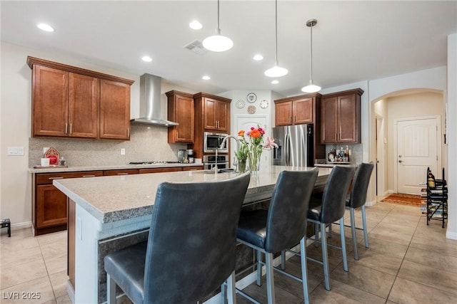 kitchen featuring backsplash, stainless steel appliances, arched walkways, light tile patterned flooring, and wall chimney range hood