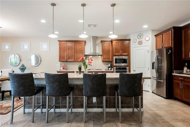 kitchen with visible vents, wall chimney range hood, a kitchen bar, appliances with stainless steel finishes, and hanging light fixtures