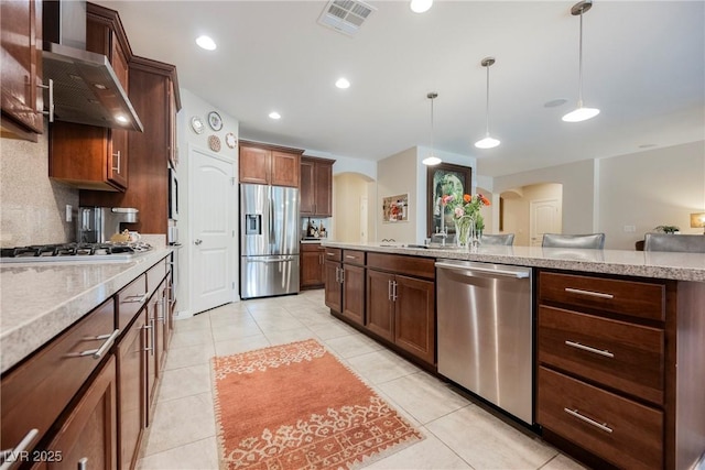 kitchen featuring visible vents, arched walkways, stainless steel appliances, pendant lighting, and wall chimney exhaust hood