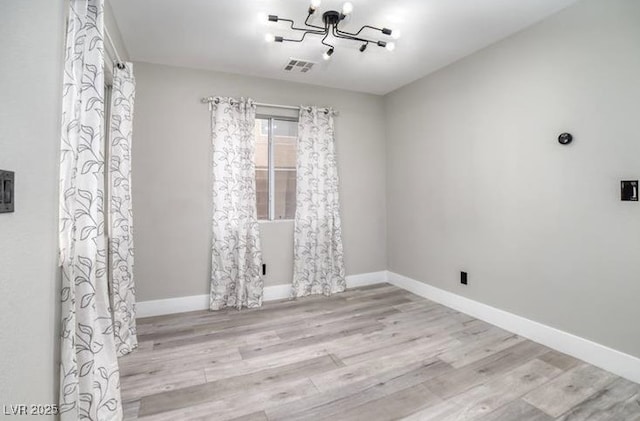 spare room featuring a chandelier, baseboards, visible vents, and wood finished floors