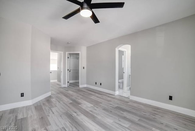 empty room featuring light wood-style flooring, baseboards, arched walkways, and ceiling fan