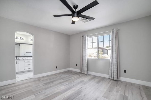 spare room featuring visible vents, light wood-style flooring, arched walkways, baseboards, and ceiling fan