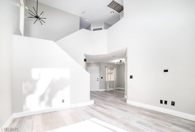 spare room with visible vents, wood finished floors, baseboards, a chandelier, and a high ceiling