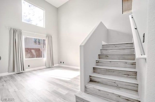 stairs with baseboards, a towering ceiling, and wood finished floors