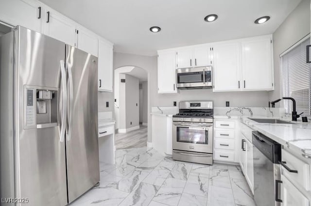 kitchen featuring light stone countertops, appliances with stainless steel finishes, arched walkways, marble finish floor, and a sink