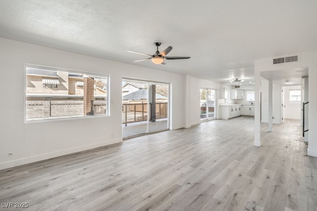 unfurnished living room with visible vents, a textured ceiling, light wood-style floors, baseboards, and ceiling fan