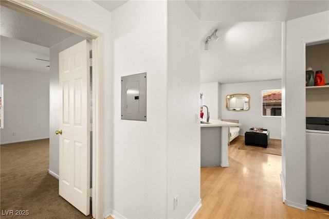 corridor featuring electric panel, light wood-type flooring, baseboards, and washer / dryer