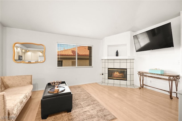 living area with a tile fireplace, baseboards, and wood finished floors