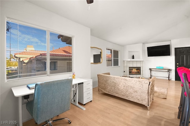 office space featuring a tiled fireplace, light wood finished floors, and vaulted ceiling