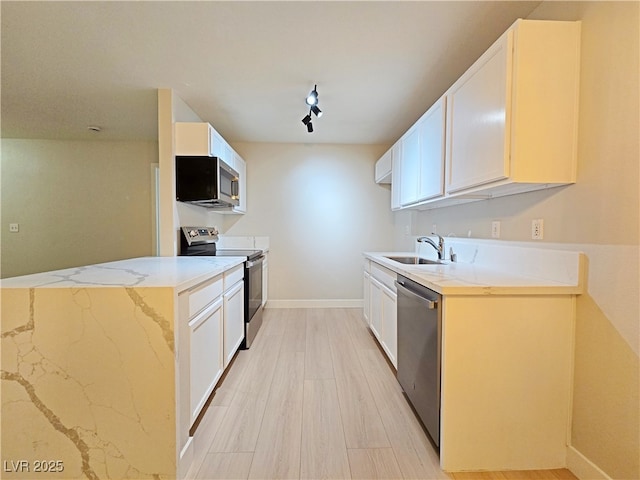 kitchen featuring light stone counters, light wood-style flooring, a sink, white cabinets, and appliances with stainless steel finishes