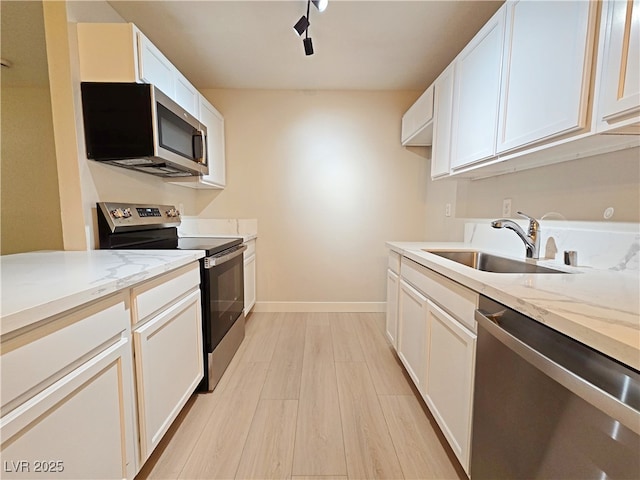 kitchen with light stone countertops, light wood-style flooring, a sink, stainless steel appliances, and white cabinetry