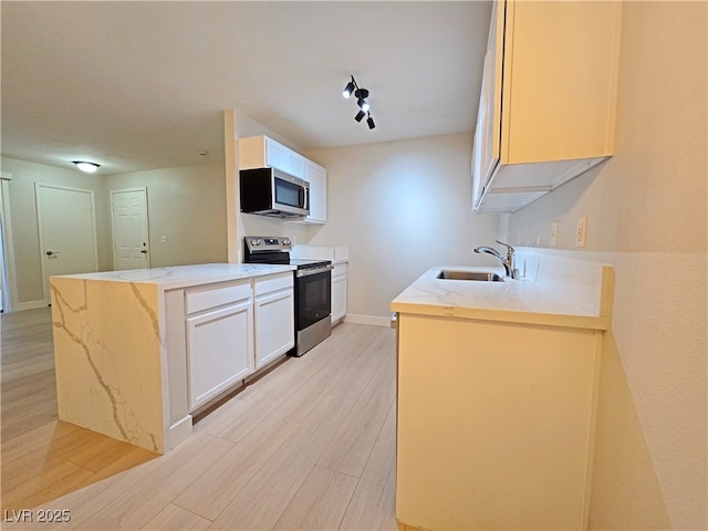 kitchen featuring light wood-type flooring, a sink, appliances with stainless steel finishes, a peninsula, and light stone countertops