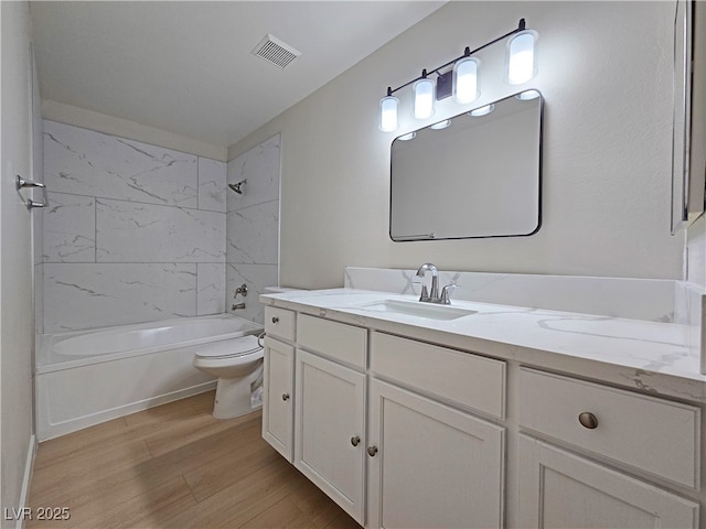 full bath featuring visible vents, toilet, vanity, wood finished floors, and washtub / shower combination