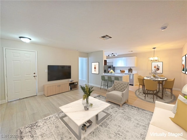 living room with visible vents, light wood-style flooring, baseboards, and an inviting chandelier