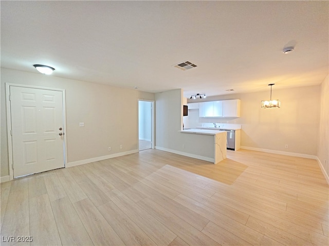 unfurnished living room featuring visible vents, baseboards, a notable chandelier, and light wood finished floors