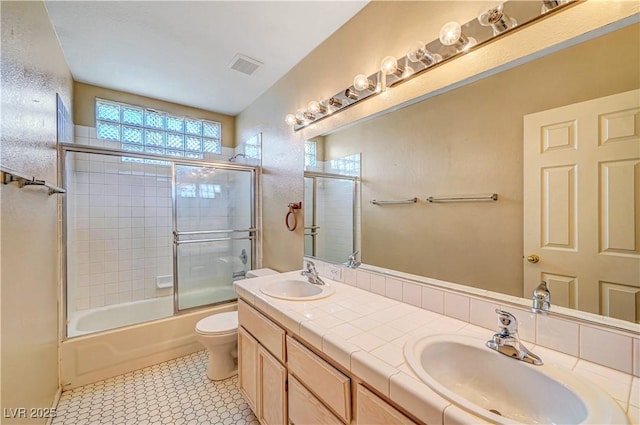 full bath featuring a sink, visible vents, toilet, and bath / shower combo with glass door