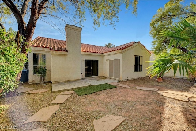 rear view of property with stucco siding, a patio, a chimney, and a tile roof