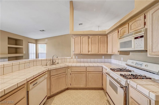 kitchen featuring white appliances, tile countertops, a peninsula, a sink, and light brown cabinetry