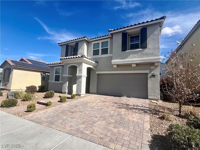 mediterranean / spanish house with stucco siding, a tiled roof, decorative driveway, and a garage