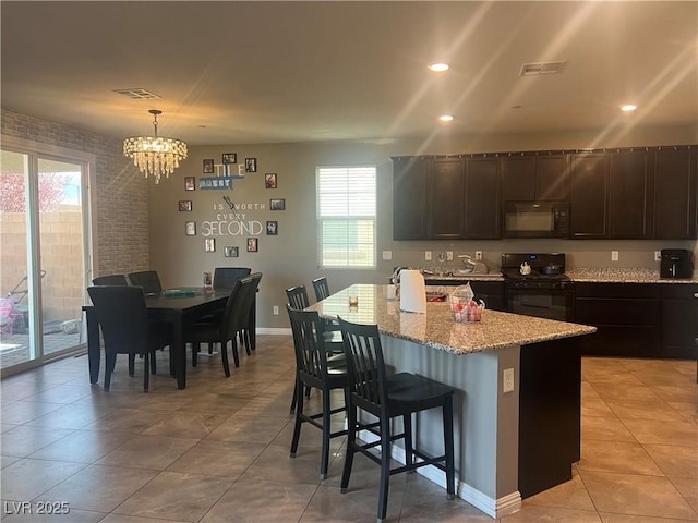 kitchen featuring a kitchen bar, visible vents, black appliances, an island with sink, and light stone counters