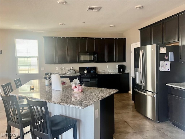 kitchen featuring visible vents, a center island, a kitchen bar, light stone counters, and black appliances