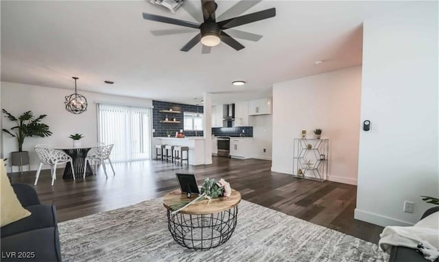 living room featuring ceiling fan with notable chandelier, baseboards, and dark wood-style flooring