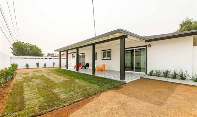 rear view of house featuring a patio, fence, a lawn, and stucco siding