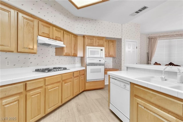 kitchen with under cabinet range hood, visible vents, white appliances, and wallpapered walls