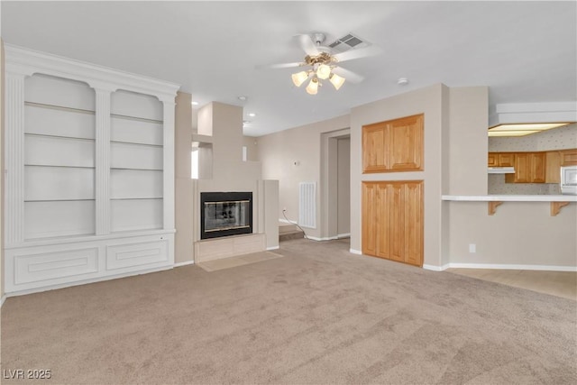 unfurnished living room with a ceiling fan, baseboards, visible vents, a fireplace, and light colored carpet