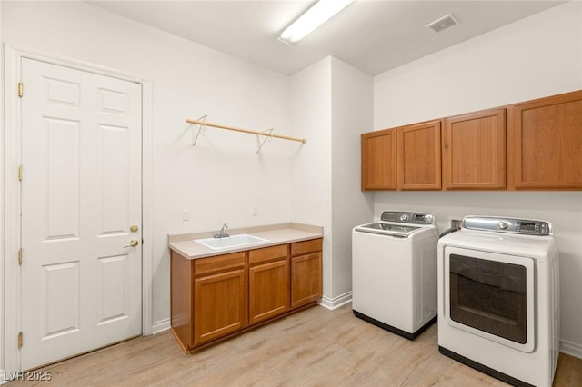 clothes washing area featuring visible vents, light wood finished floors, washing machine and clothes dryer, cabinet space, and a sink