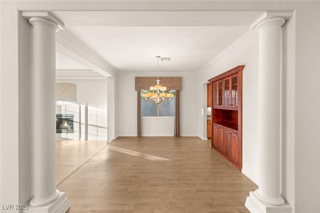 unfurnished dining area featuring crown molding, decorative columns, light wood finished floors, and a lit fireplace