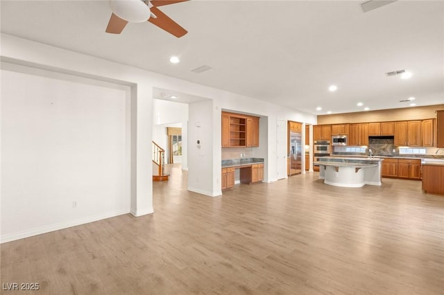 unfurnished living room with light wood-type flooring, visible vents, a sink, recessed lighting, and baseboards