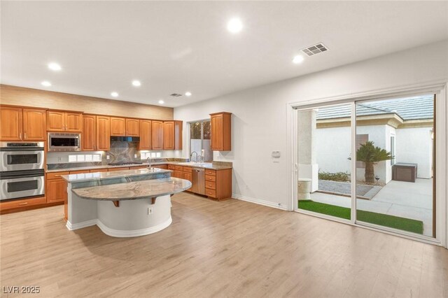 kitchen with visible vents, appliances with stainless steel finishes, light wood-type flooring, and a kitchen island with sink