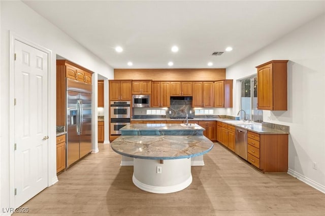 kitchen featuring built in appliances, a center island with sink, brown cabinets, and visible vents