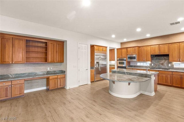 kitchen with visible vents, light wood-style flooring, built in desk, built in appliances, and brown cabinets