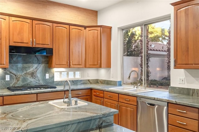 kitchen featuring under cabinet range hood, light stone countertops, stainless steel appliances, and a sink