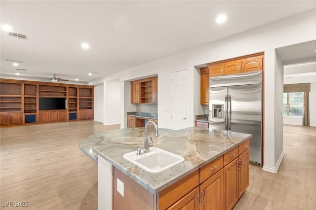 kitchen with visible vents, a kitchen island with sink, a sink, light wood-style floors, and built in fridge