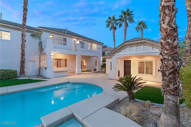 rear view of property featuring a patio, a balcony, an outdoor pool, and stucco siding