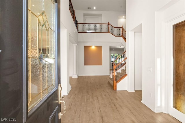 foyer with wood finished floors, baseboards, ornamental molding, stairs, and a towering ceiling