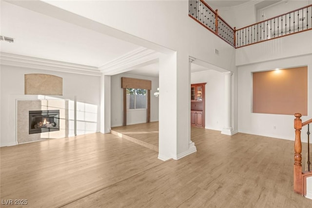 unfurnished living room featuring a high end fireplace, crown molding, wood finished floors, and ornate columns