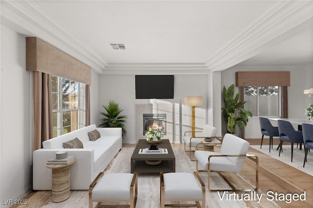 living area with a tile fireplace, visible vents, a wealth of natural light, and ornamental molding