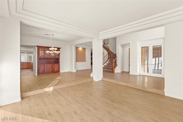 unfurnished living room featuring light wood finished floors, stairs, ornamental molding, french doors, and an inviting chandelier