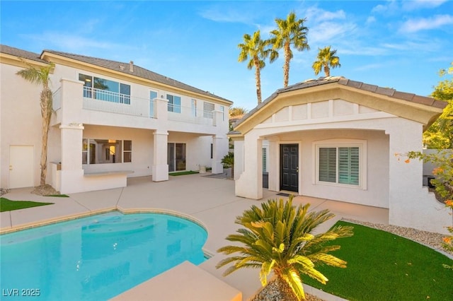 back of property featuring a patio, a balcony, an outdoor pool, and stucco siding